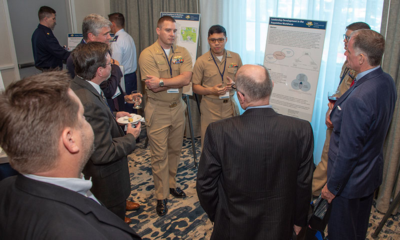 Lt. Cmdr. Andrew Foursha, left, and Lt. Raymond-Victor Pajarillo presented to attendees at the Acquisition Research Symposium.